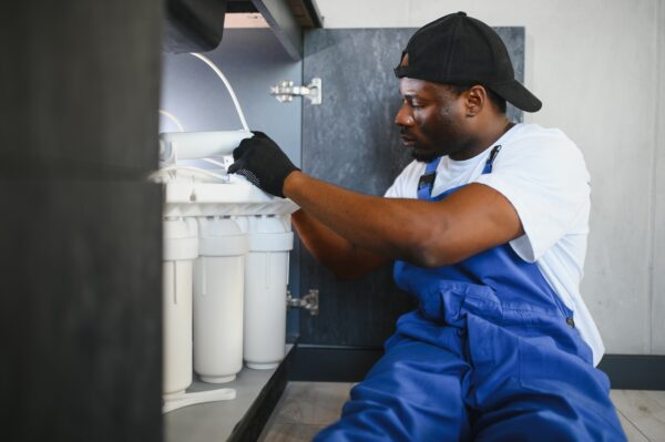 A man in a backward cap installs a new house water filtration system in Overland Park