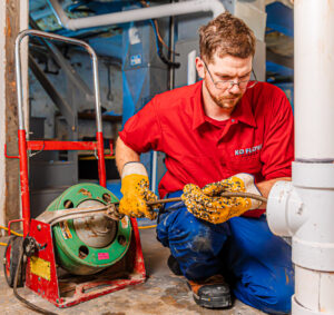 A team member crouches and inspects a pipe as her performs drain cleaning in Johnson County.